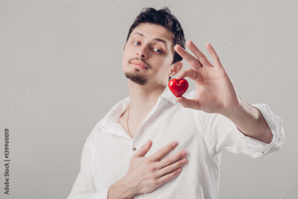 handsome young brunette man in shirt holds in hands red heart on