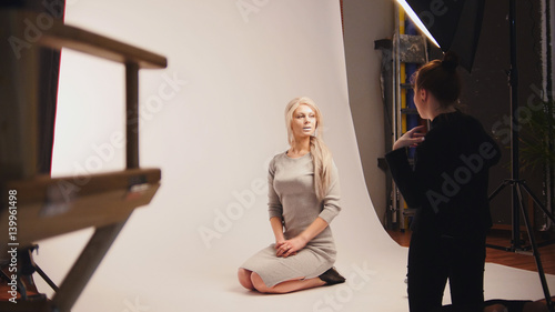 Fashion photo backstage - Blonde handsome girl posing for photographer - model sits at knees