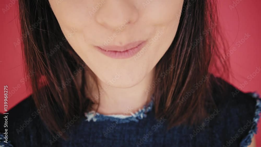 Close up front view, unrecognizable brunette girl with big smile and white healthy teeth bites white macaron cookie, isolated on red background Close up front view, unrecognizable brunette girl with big smile and white healthy teeth bites white macaron cookie, isolated on red background