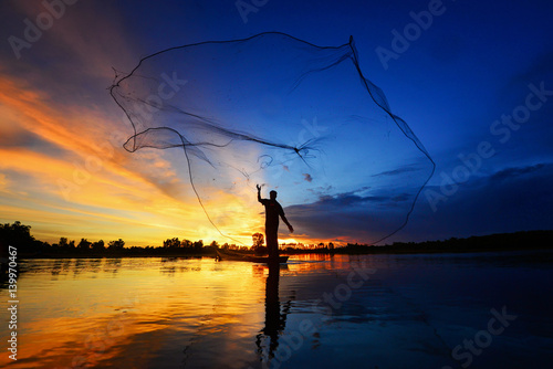 The silluate fisherman trowing the nets  on boat in river  at during sunset,Thailand fisherman,fisherman nets,fisherman sunset photo
