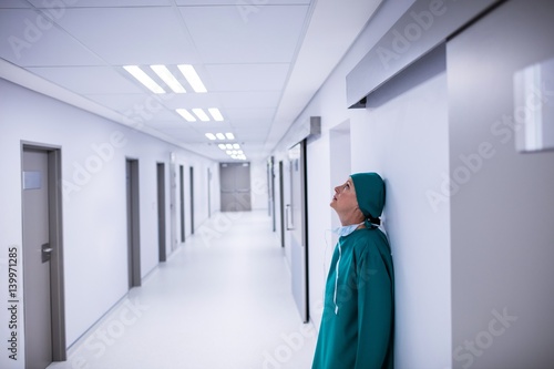 Tensed female surgeon leaning on wall in corridor