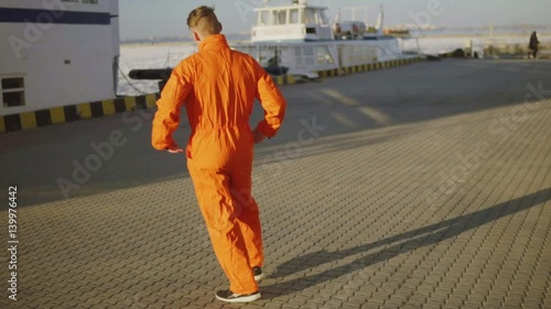 Young harbor worker in orange uniform is turnng around in the sun. Happy young man is celebrating something. photo