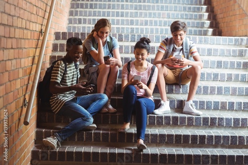 Classmates sitting on staircase and using mobile phone