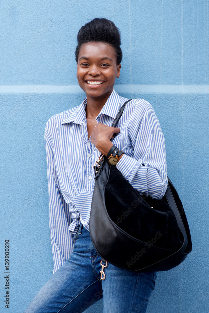 Fototapeta premium african american woman smiling with handbag against blue wall