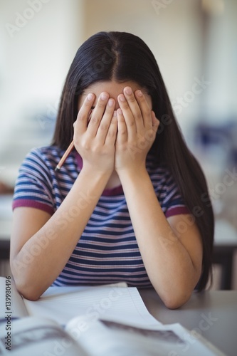 Stressed schoolgirl doing covering her face in classroom