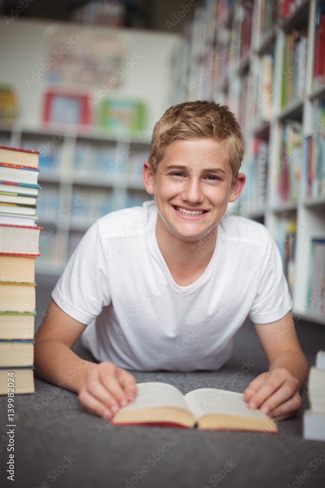 Portrait of happy schoolboy lying on floor with books in library Portrait of happy schoolboy lying on floor with books in library