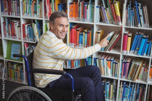 Portrait of disabled school teacher selecting book in library