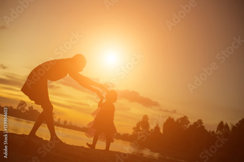 Silhouettes of mother and little daughter walking at sunset