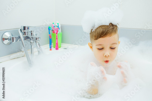 Happy young boy taking a bath. Child washes in the foam.