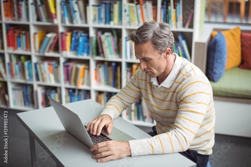 Attentive school teacher using laptop in library