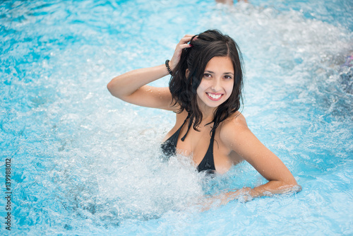 Young brunette female in a black bathing suit with a snow-white smile relaxing in a jacuzzi