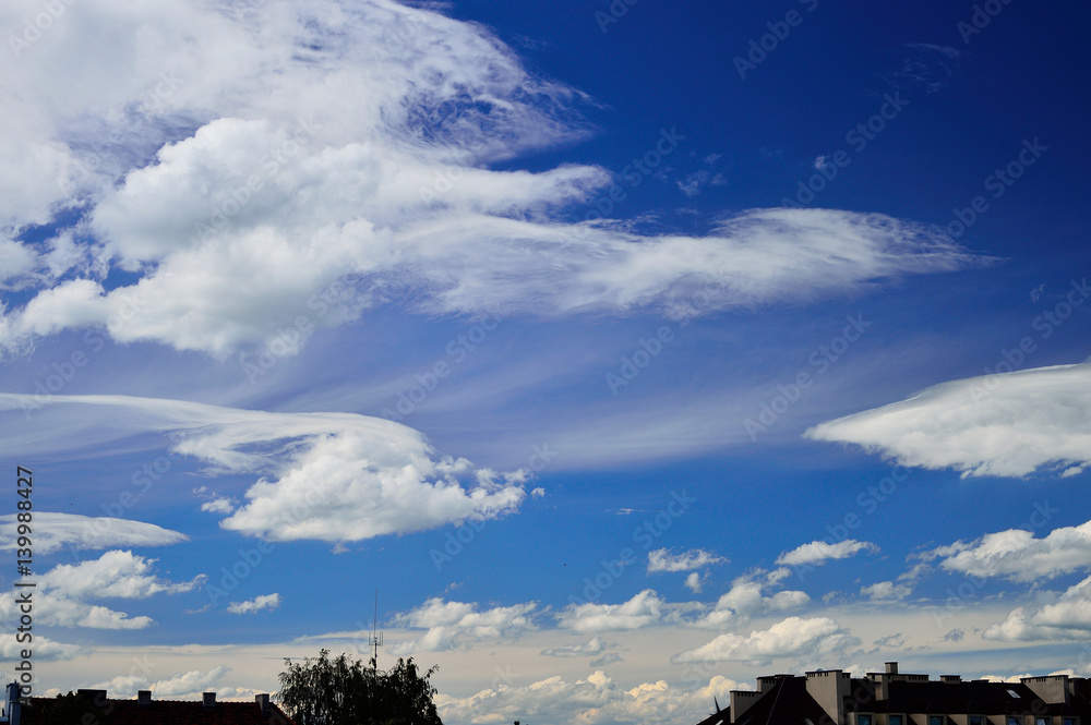 Fototapeta premium Chmury na błękitnym niebie nad budynkami mieszkalnymi.