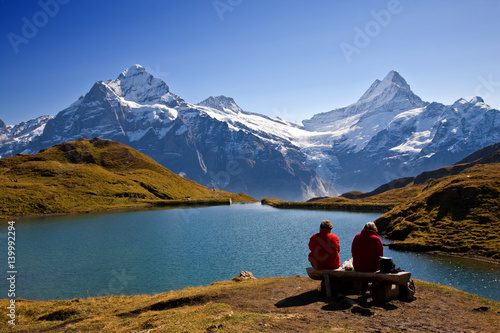 Swiss hikers (red jackets) on a picnic overlooking lake and Wetterhorn mountain. High above Grindelwald.