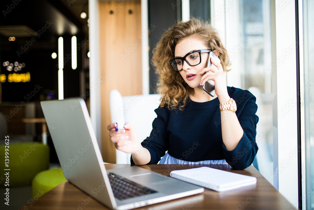 Young business woman at coworking speak at phone and make notice in notebook Young business woman at coworking speak at phone and make notice in notebook