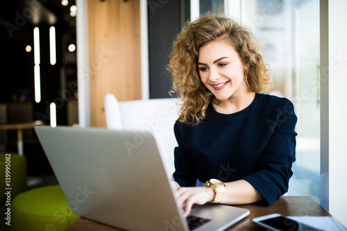 фотографія Happy curlu young woman use laptop in modern place with bright windows
