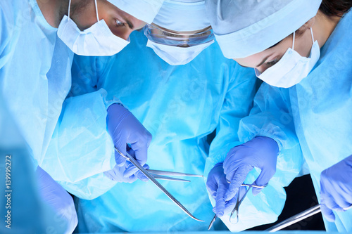 Medical team performing operation. Group of surgeons at work in operating theater toned in blue