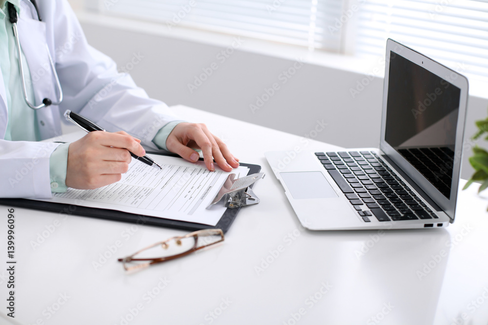 Close-up of a female doctor filling out application form , sitting at the table in the hospital Close-up of a female doctor filling out application form , sitting at the table in the hospital