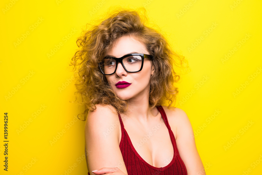 Beauty portrait of young american girl with curly hairstyle. Girl posing on yellow background, looking at camera, smiling. Studio shot. Beauty portrait of young american girl with curly hairstyle. Girl posing on yellow background, looking at camera, smiling. Studio shot.