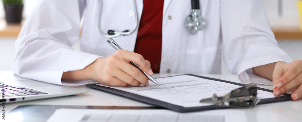 Close up of unknown female doctor typing on laptop computer while sitting at the table. Medical staff, compulsory work concept Close up of unknown female doctor typing on laptop computer while sitting at the table. Medical staff, compulsory work concept