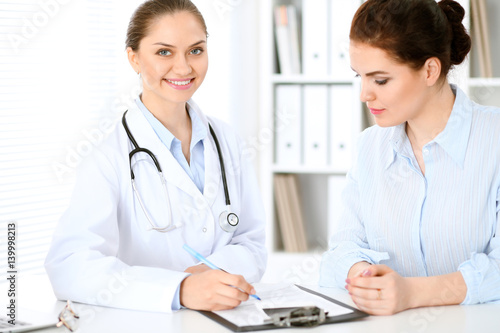 Friendly smiling doctor and patient sitting at the table. Very good news and high level medical service concept.