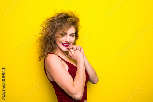Young beautifulgirl with an curly hairstyle. Laughing girl take selfie from phone on Yellow background.