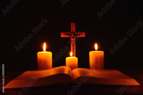 Obraz na płótnie Crucifix and three burning candles with open bible on table in the darkness. Pray to Jesus Christ. Hope on good life. 4 w salonie