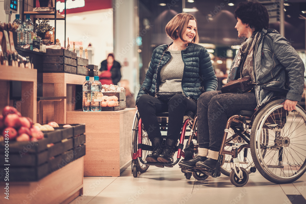 Two smiling disabled women in wheelchair in a department store Two smiling disabled women in wheelchair in a department store