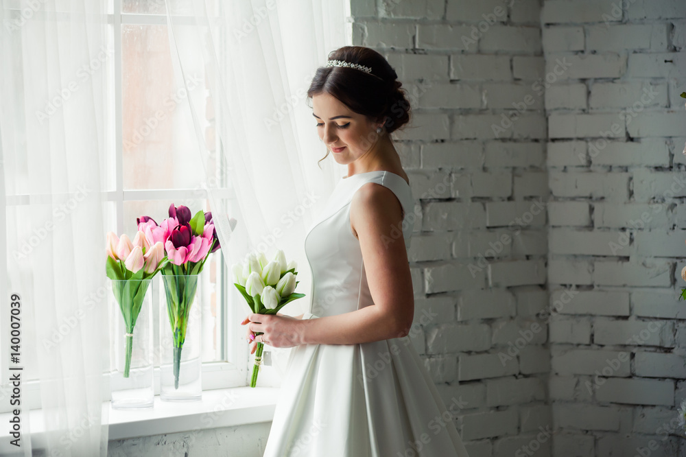 Beautiful bride with bouquet before wedding ceremony near window Beautiful bride with bouquet before wedding ceremony near window