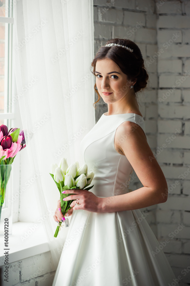 Beautiful bride with bouquet before wedding ceremony near window Beautiful bride with bouquet before wedding ceremony near window