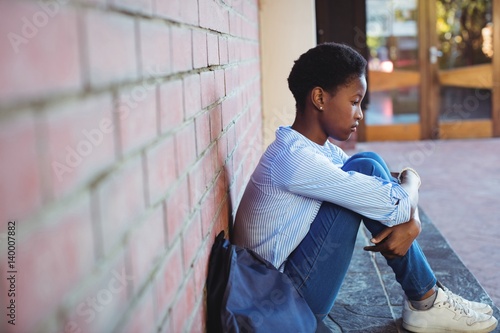 Canvas Print Sad schoolgirl sitting against brick wall