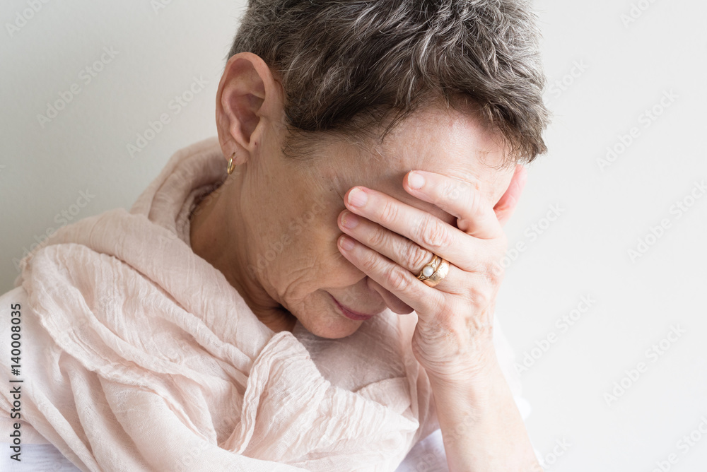 Older woman with short hair and cream scarf looking down with hand over eyes (selective focus) Older woman with short hair and cream scarf looking down with hand over eyes (selective focus)