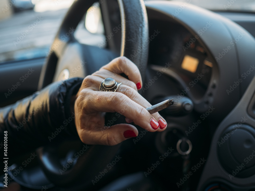 Cigarette in the hand with steering wheel of car