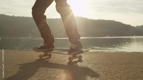 SLOW MOTION, CLOSE UP: Unrecognizable skateboarder skateboarding and jumping nollie kickflip trick on pavement along the ocean at golden light sunset. Skateboarder doing skateboard tricks by the sea photo