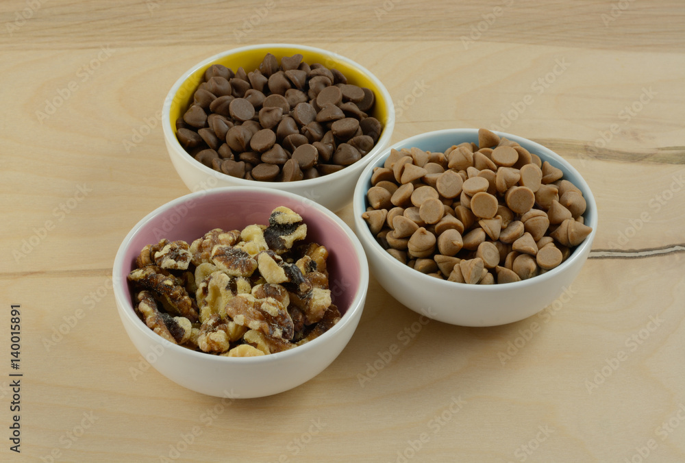 Chocolate chips, peanut butter chips and walnut toppings in bowls Chocolate chips, peanut butter chips and walnut toppings in bowls