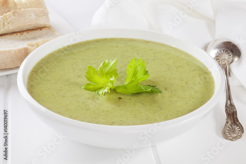 A bowl of creamy celery soup with a garnish of celery leaves, served with crusty bread.