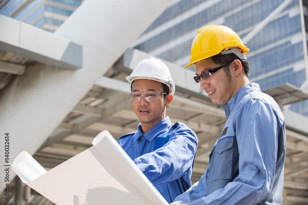 Engineer and Foreman outside office with yellow, white helmet point to building in the city with a blank plan as for construction, Teamwork Concept Engineer and Foreman outside office with yellow, white helmet point to building in the city with a blank plan as for construction, Teamwork Concept