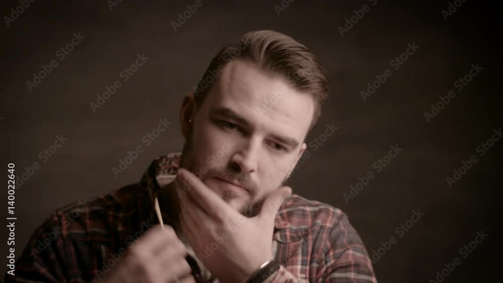 Bearded young man posing in the studio on a brown background. A man with a beard comb his beard Bearded young man posing in the studio on a brown background. A man with a beard comb his beard