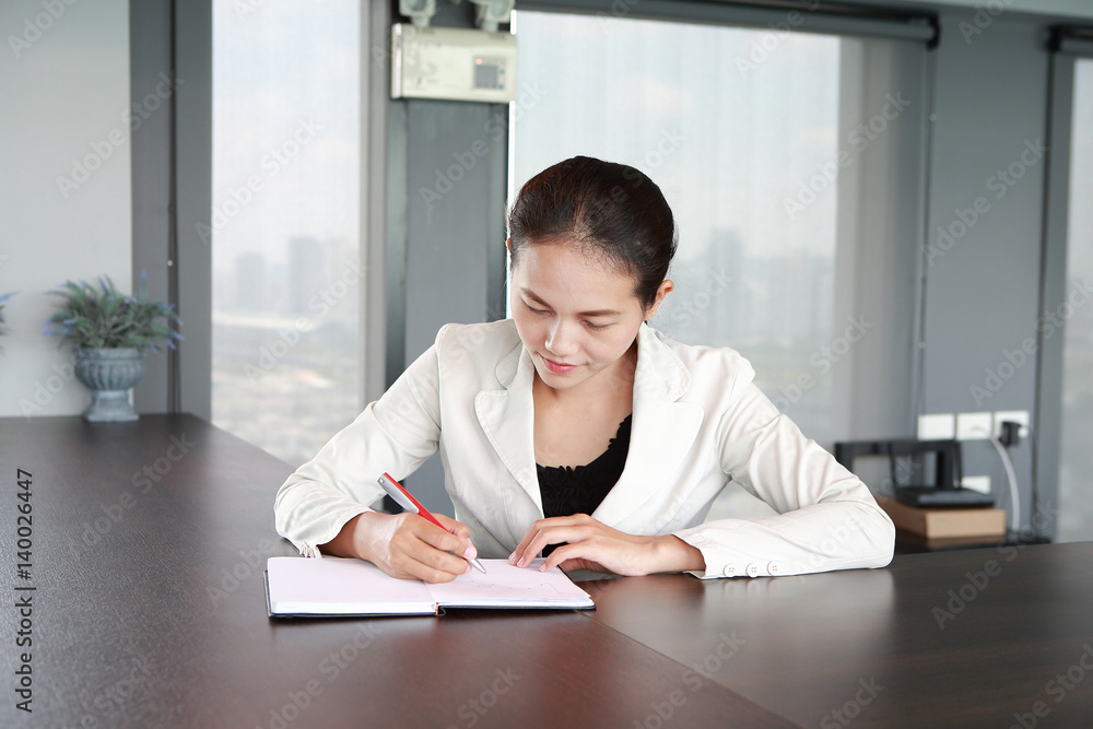 Young businesswoman sitting at the table on workplace in office and writing Young businesswoman sitting at the table on workplace in office and writing