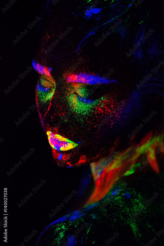 Beautiful extraterrestrial model woman in neon light. It is portrait of beautiful model with fluorescent make-up, Art design of female posing in UV with colorful make up. Isolated on black background