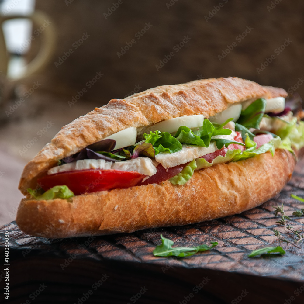 Long baguette sandwich with lettuce tomatoes eggs onion and mayo sauce served on a wooden board. Rustic style and close up. Square image. Long baguette sandwich with lettuce tomatoes eggs onion and mayo sauce served on a wooden board. Rustic style and close up. Square image.