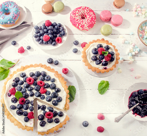 Sweet desserts with fresh berries on a white wooden table.