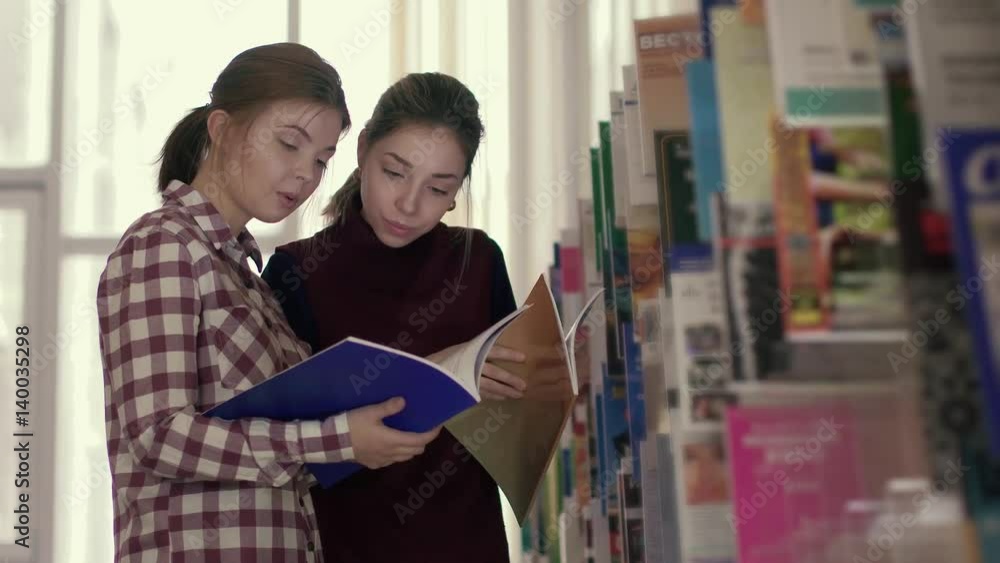 Two female students looking for necessary information in library books Two female students looking for necessary information in library books