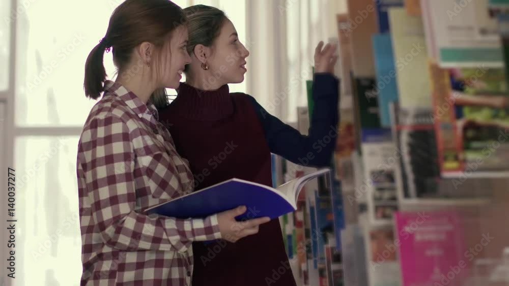 Two female students meeting in the library while looking for suitable books Two female students meeting in the library while looking for suitable books
