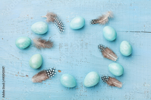 Painted Easter eggs and feather on rustic blue background top view in flat lay style. Clean space for text.