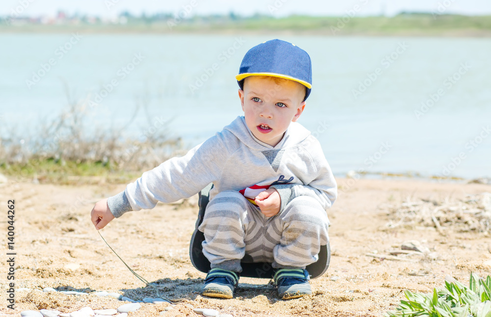 Little boy is sitting on the shore of the lake