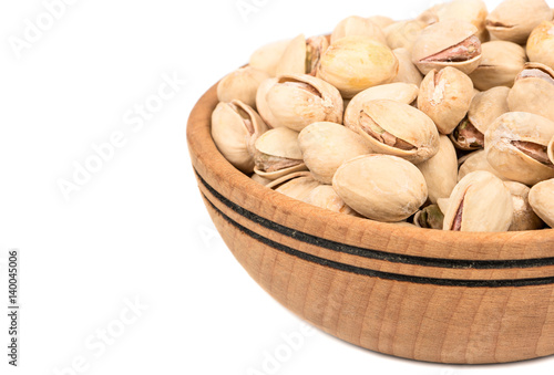 Part of a wooden bowl with pistachios on a white background, close-up