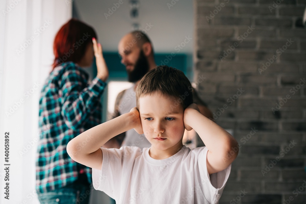 Sad child covering his ears with hands during parents quarrel.