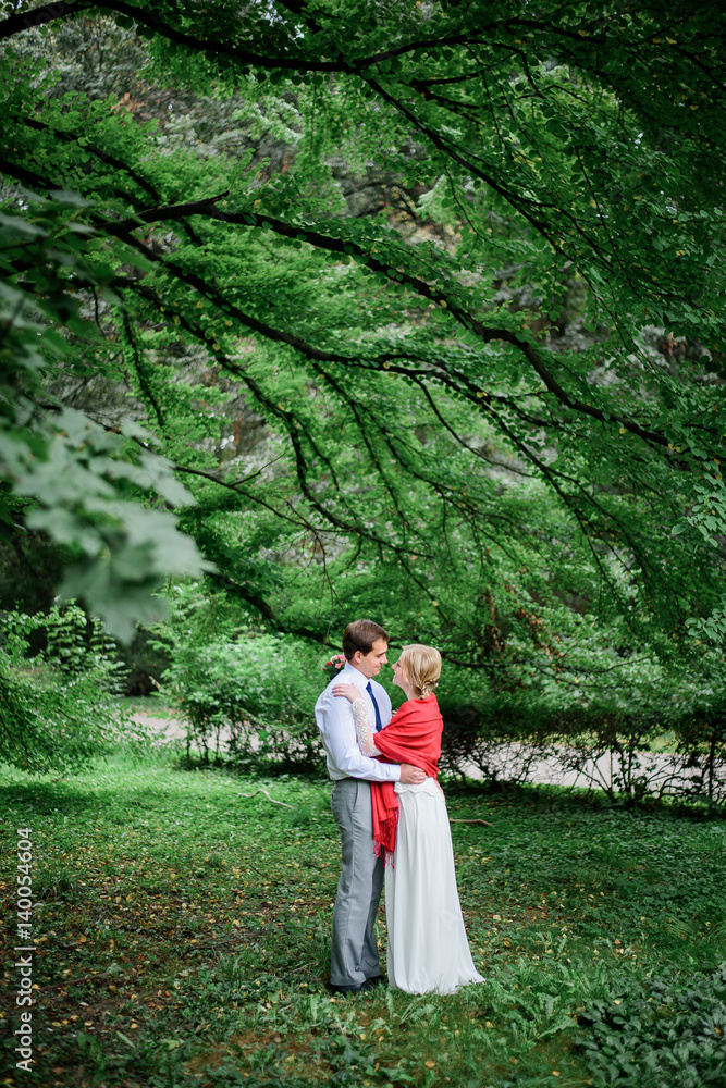 Man hugs tender lady with red shawl on her shoulders in park Man hugs tender lady with red shawl on her shoulders in park