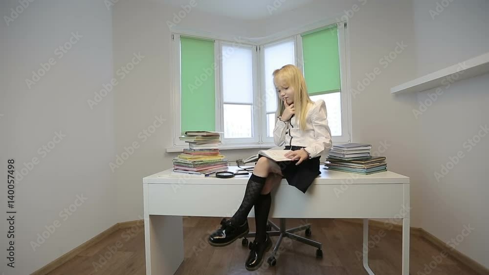 Little schoolgirl sitting on a desk and leafs through the diary. Little schoolgirl sitting on a desk and leafs through the diary.
