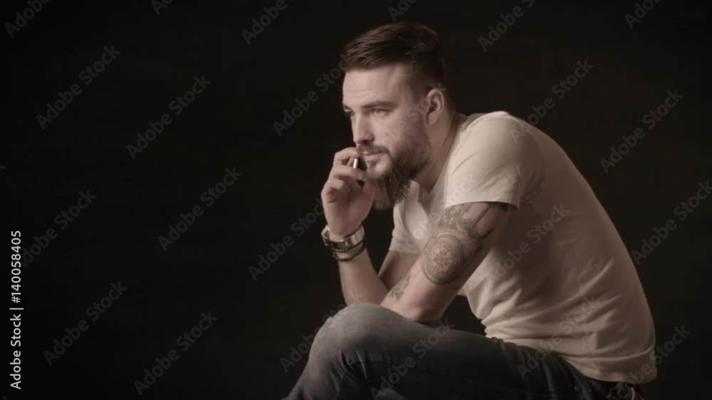 Handsome man with a beard talking on the phone in a studio on a black background